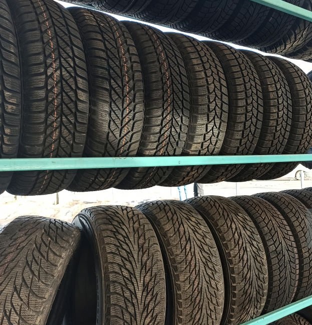 Many black rubber car tires on store shelf for sale.